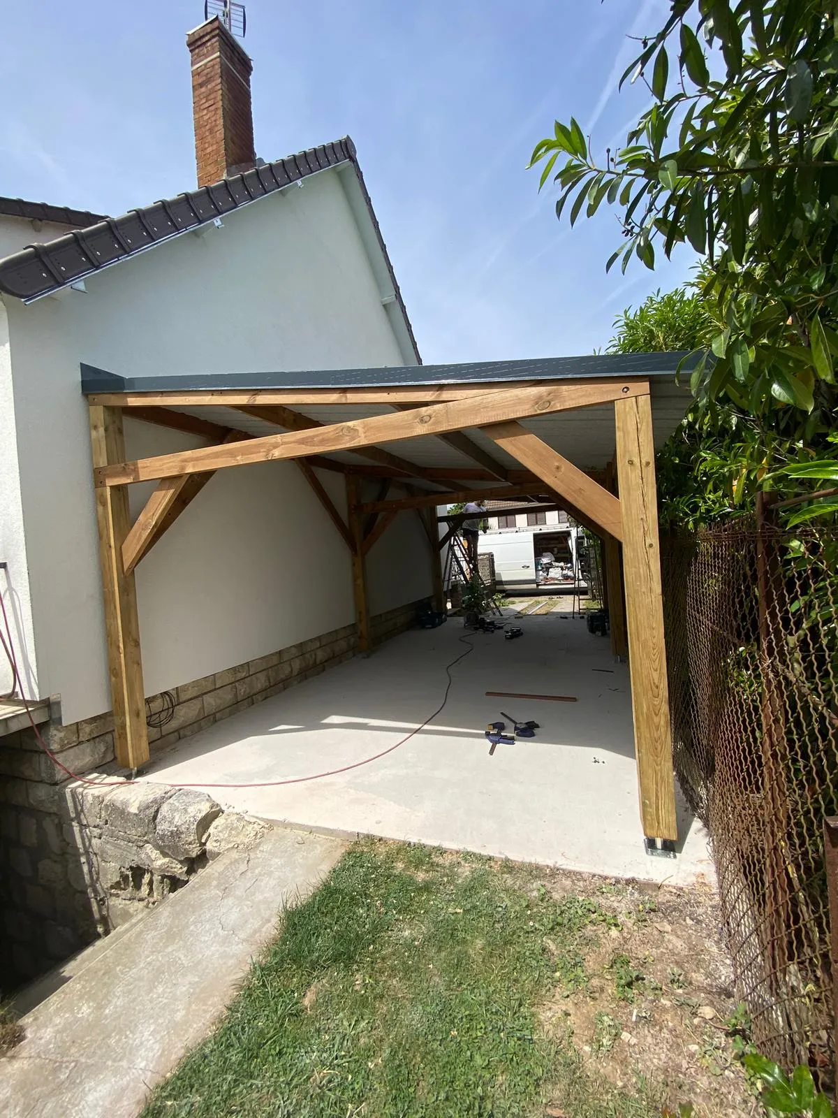 Structure d'un carport bois autoporté à toiture bac acier sous ciel bleu, à Crépy-en-Valois dans l'Oise