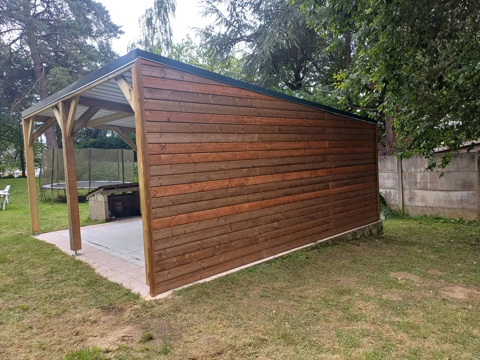 Carport bois avec mur en bardage bois lasuré, vue arrière dans un jardin de l'Aisne