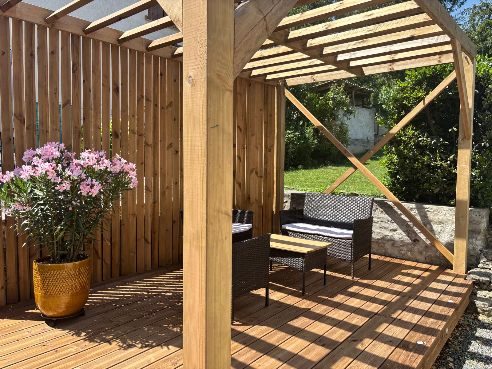 Pergola bois en pin à lames fixes avec brise-vue à lames verticales et salon de jardin, posée sur une terrasse en bois, réalisée par La Planète Bois