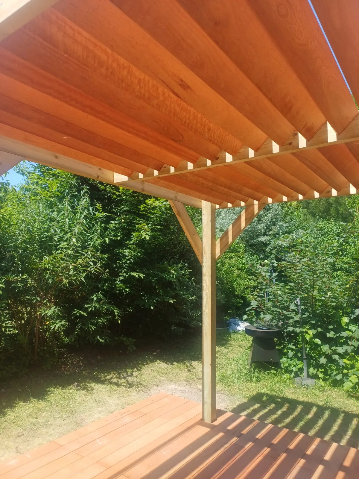 Vue par dessous de la toiture à chevrons en bois d'une pergola adossée, lumière chaude sur le bois, réalisée par La Planète Bois