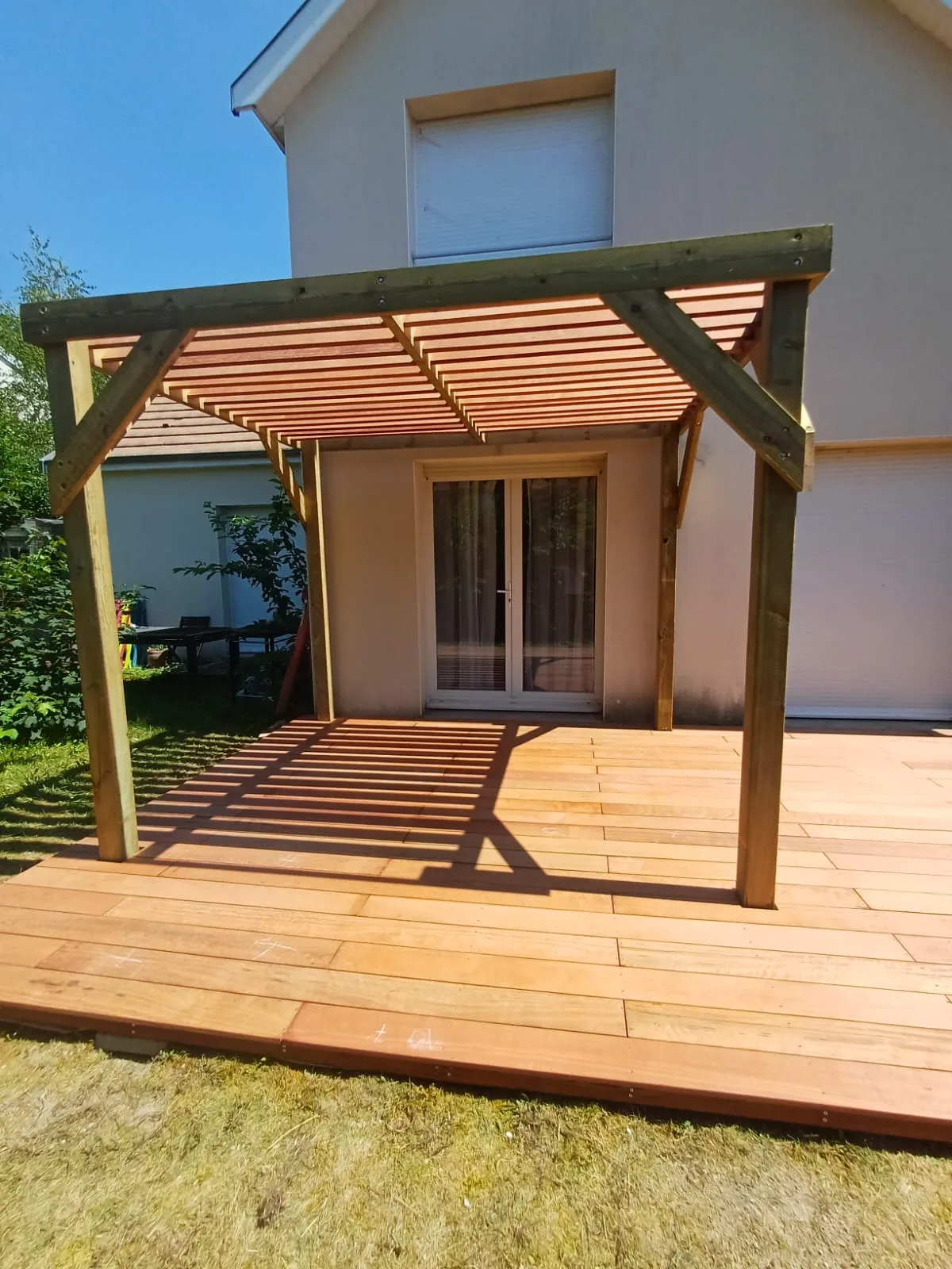 Pergola bois adossée à la façade vue de face, posée sur une terrasse en bois exotique dans un jardin, réalisée par La Planète Bois