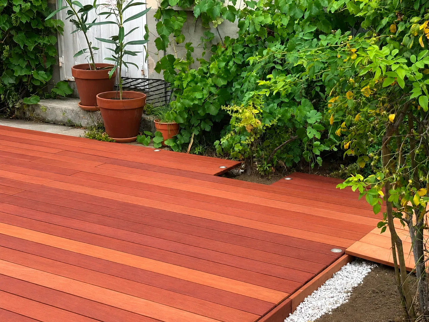 Détail des lames en bois exotique aux teintes rouge et orangé et des spots encastrés d'une terrasse à Hermonville
