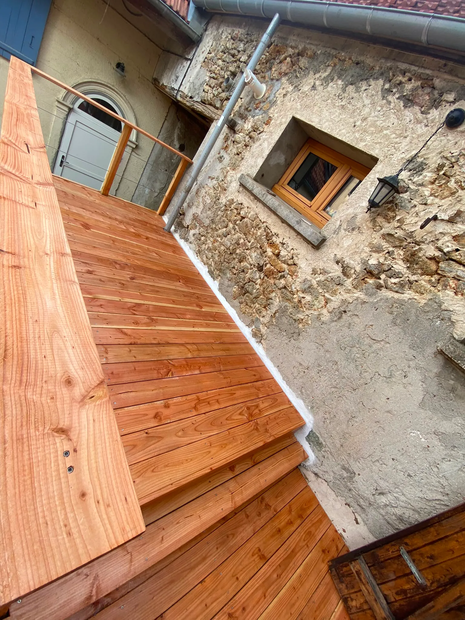Détail des lames de terrasse en bois le long d'un mur en pierre apparente, chantier réalisé en Essonne par La Planète Bois
