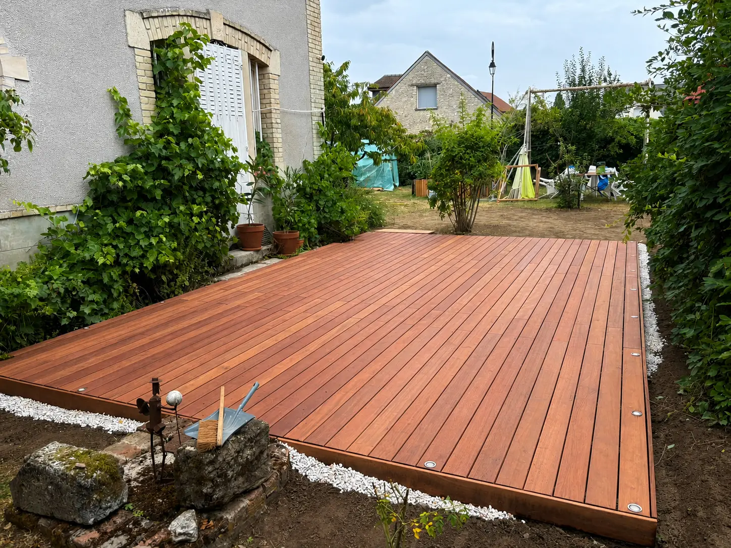 Terrasse en bois exotique sur mesure posée par La Planète Bois dans un jardin, devant une maison ancienne